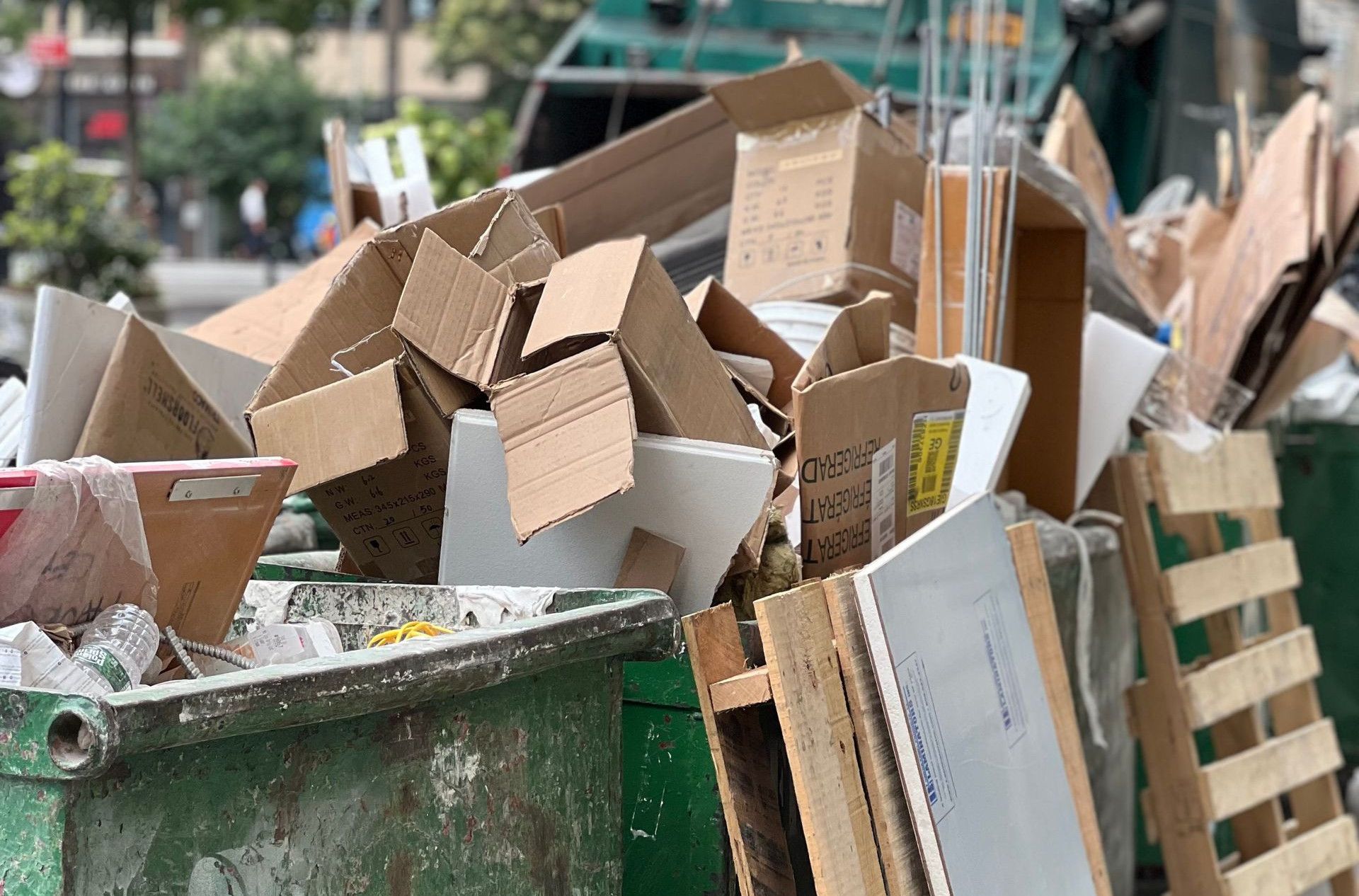 Piled cardboard boxes and waste in a city dumpster highlight urban recycling.